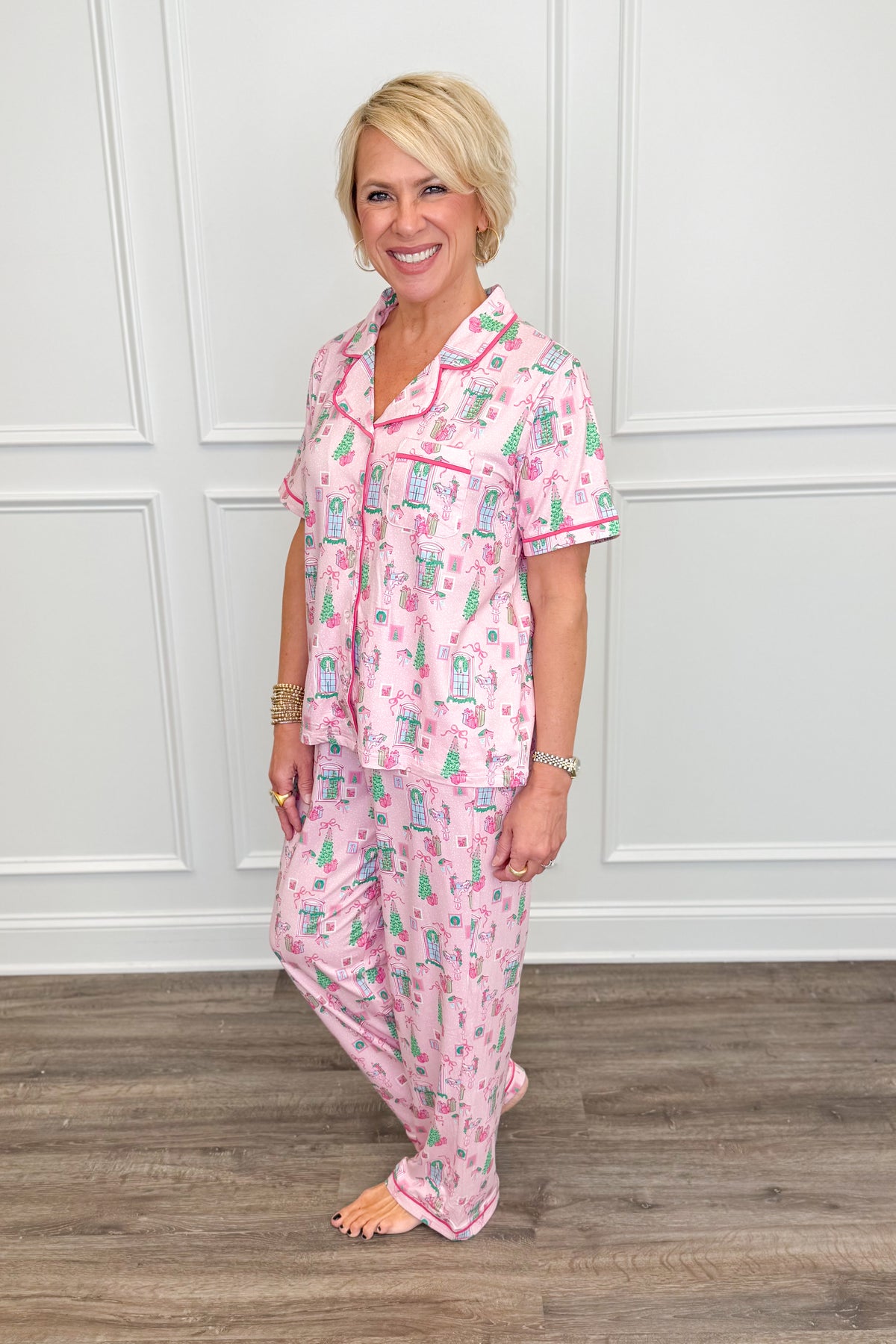 Side view of the Christmas Cottage Charlotte Pajama Set featuring a pink holiday print, short-sleeve button-down top with contrast piping, and matching long pajama pants with a relaxed, comfortable fit.