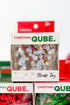 A stack of small retail boxes labeled Christmas Qube. Stress Toy, showing iridescent round confetti pieces visible through clear front windows.