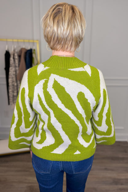 Back view of woman wearing Swagger Boutique’s Citron Zebra Mock Neck Sweater by Entro with jeans with clothing hanging in the background.