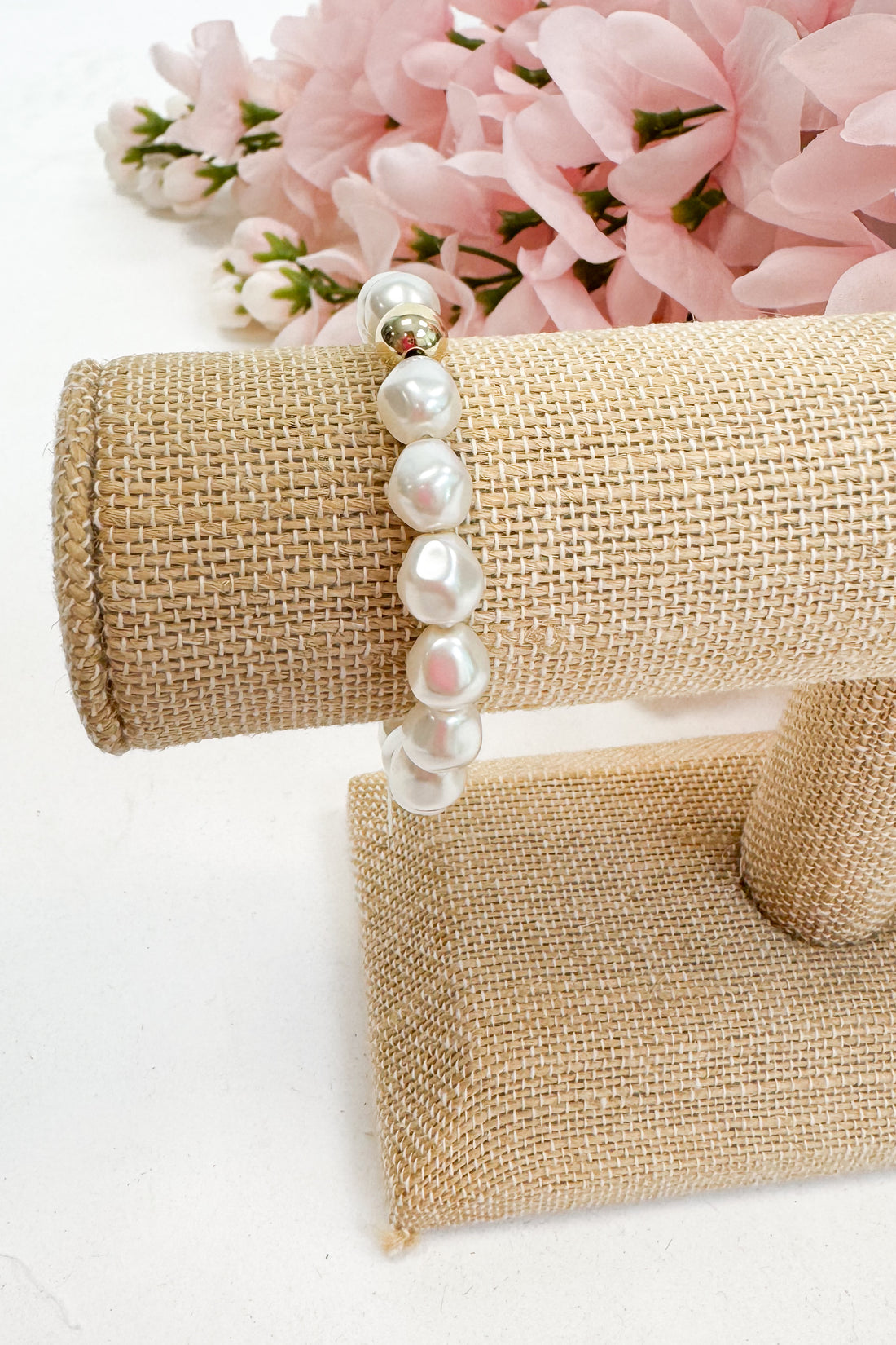 Pearl bracelet on a beige jewelry stand with pink flowers in the background
