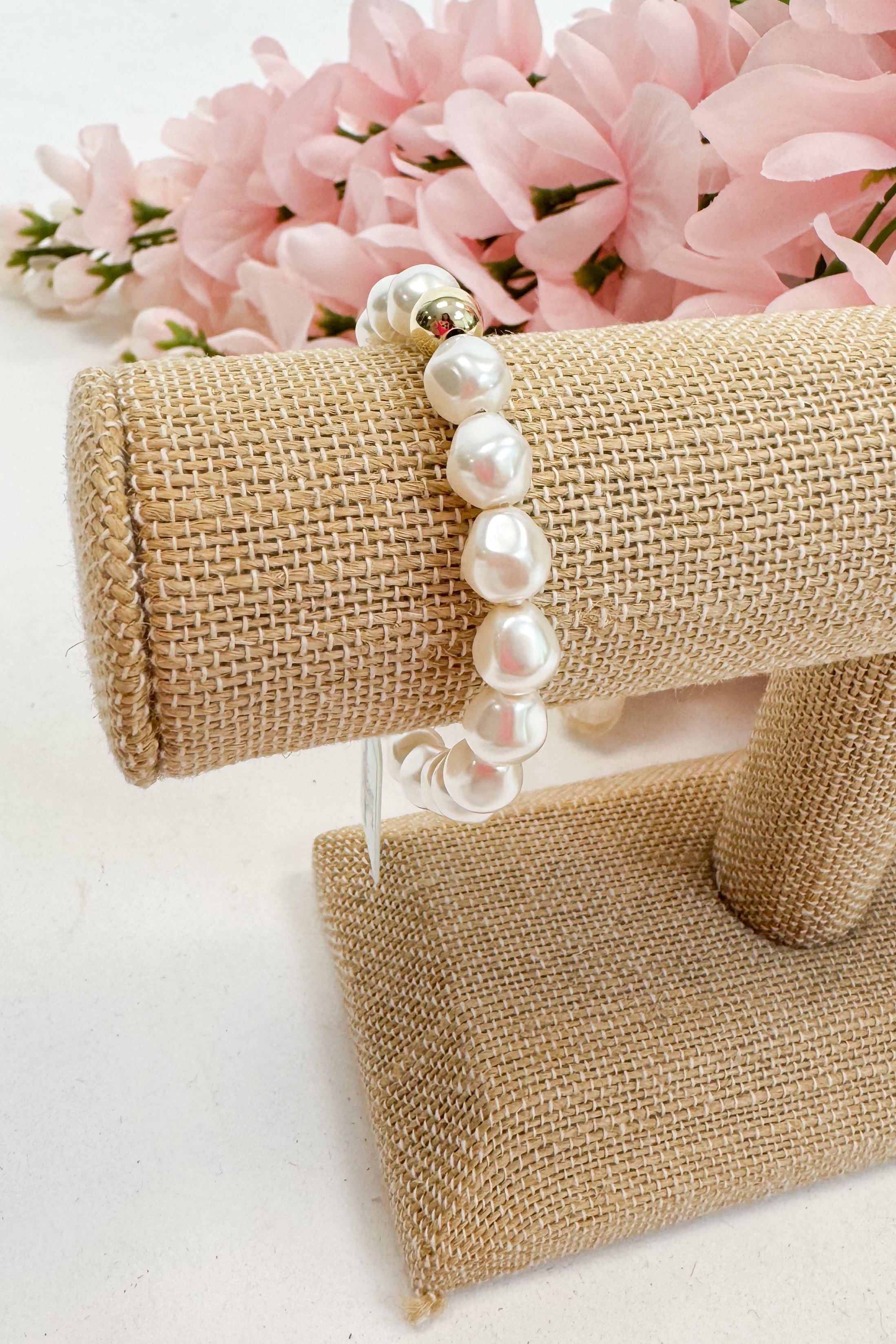 Pearl bracelet on a burlap stand with pink flowers in the background