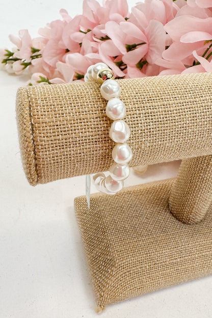 Pearl bracelet on a burlap stand with pink flowers in the background