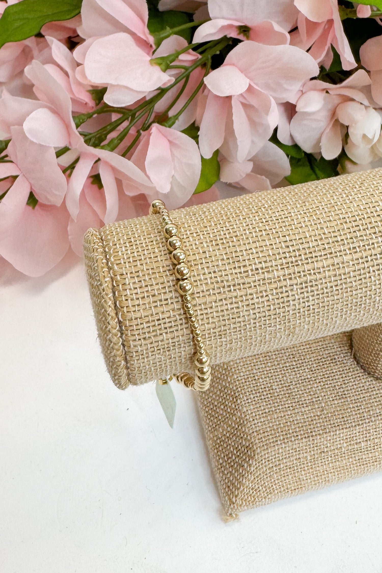 Gold bracelet on a burlap roll with pink flowers in the background