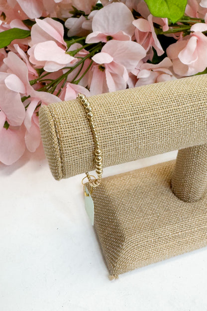 Gold bracelet on a beige jewelry display with pink flowers in the background