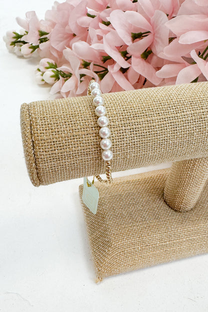 Pearl bracelet on a beige stand with pink flowers in the background
