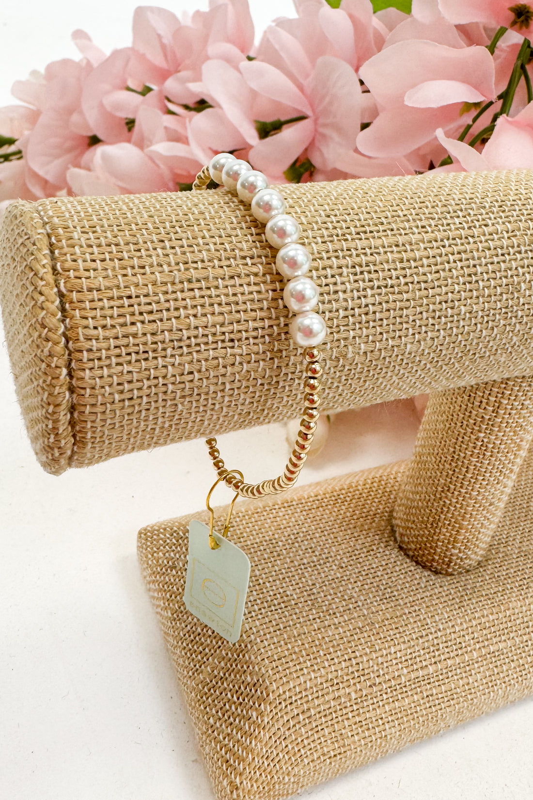 Pearl bracelet on a burlap display with pink flowers in the background