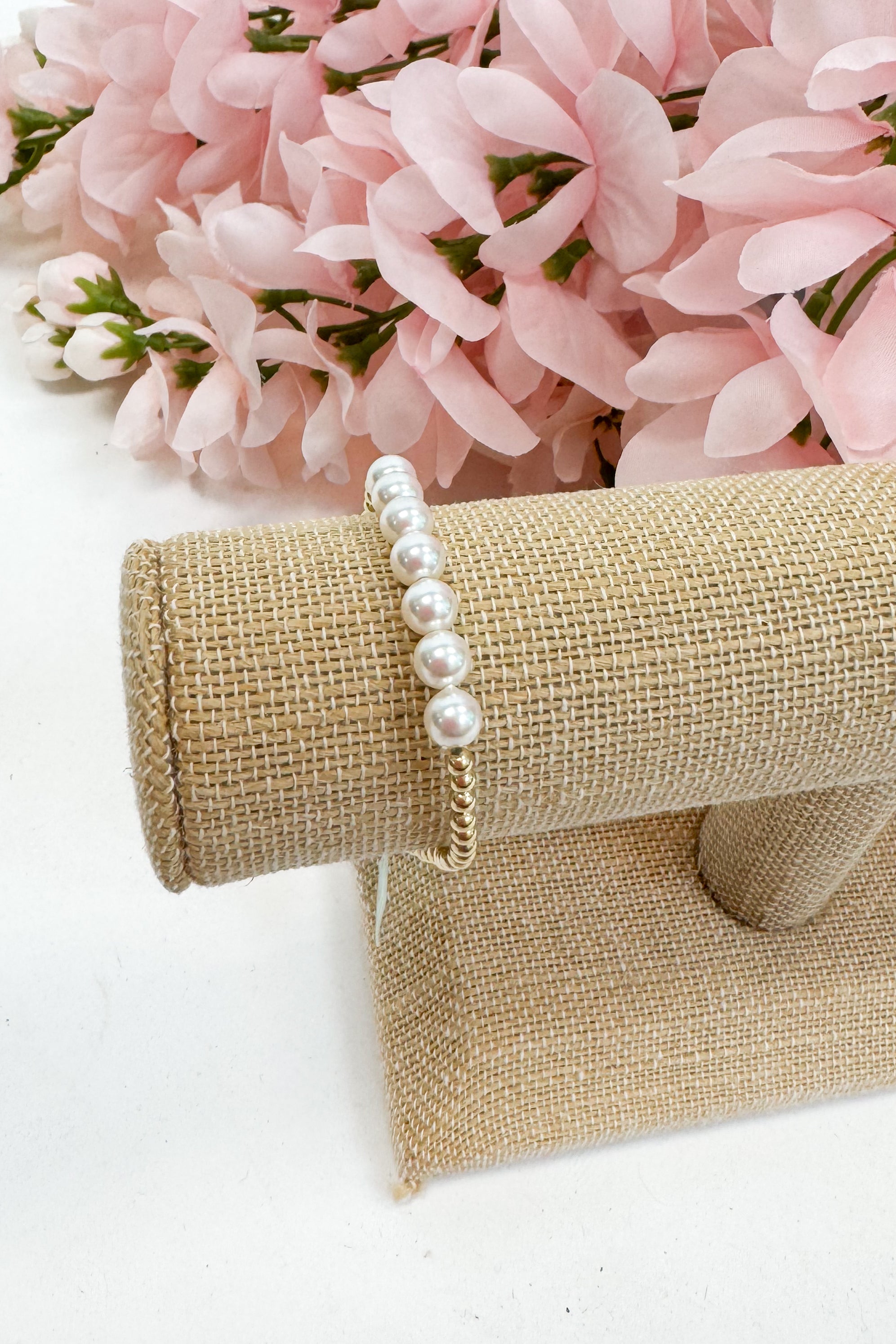Pearl bracelet on a burlap roll with pink flowers in the background