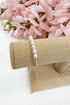 Pearl bracelet on a burlap roll with pink flowers in the background