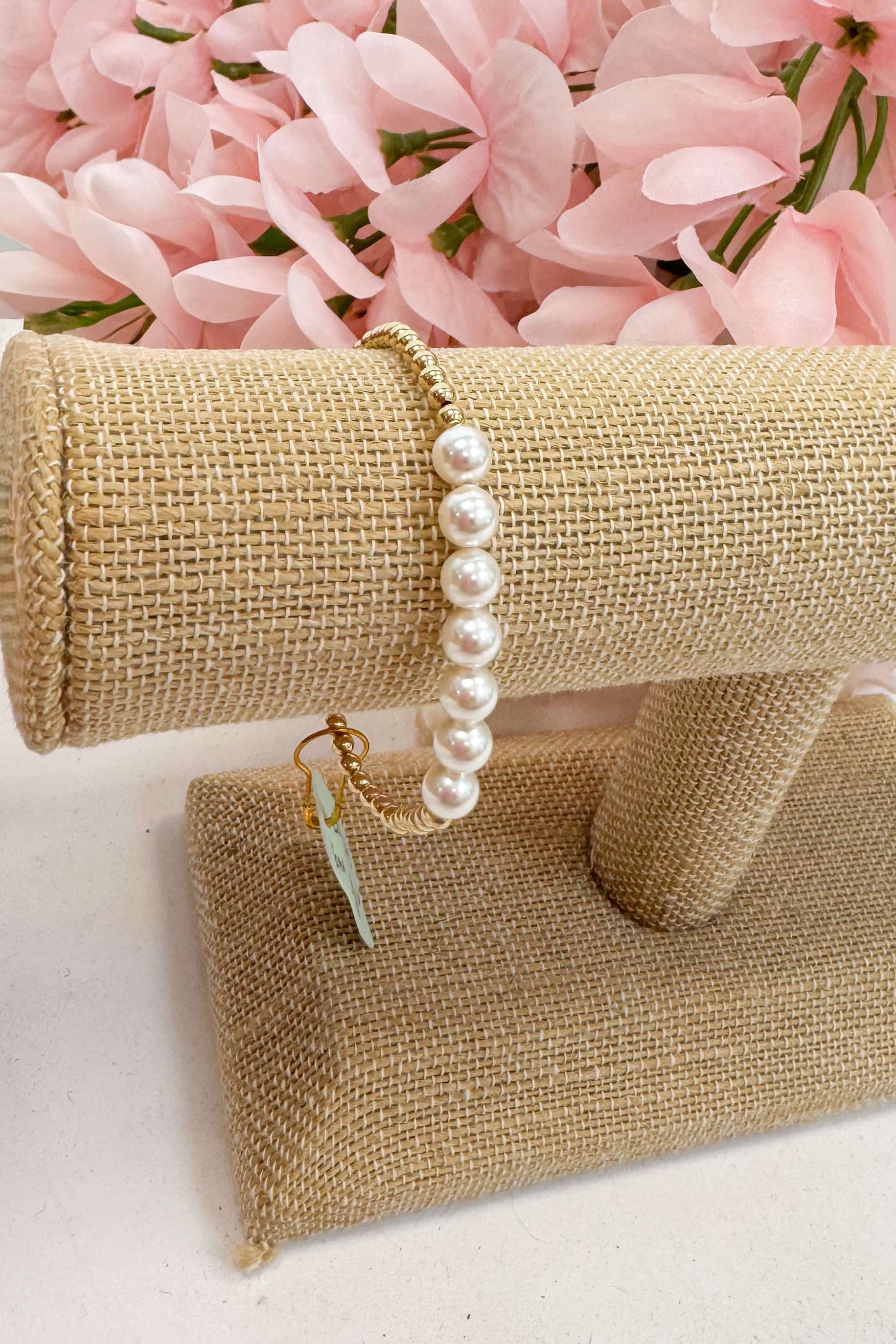 Pearl bracelet on a beige jewelry display with pink flowers in the background
