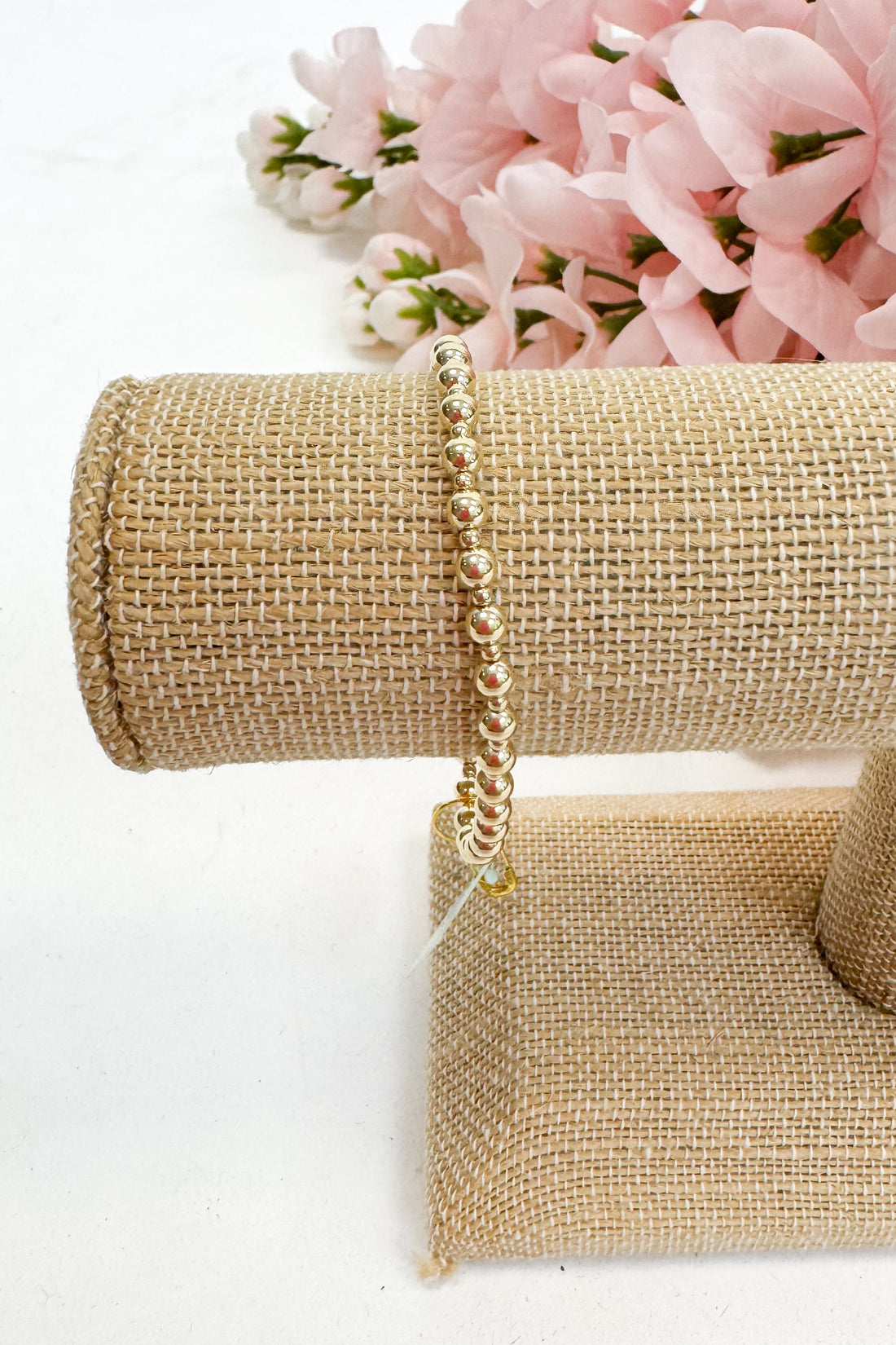 Gold bracelet on a gold jewelry stand with pink flowers in the background