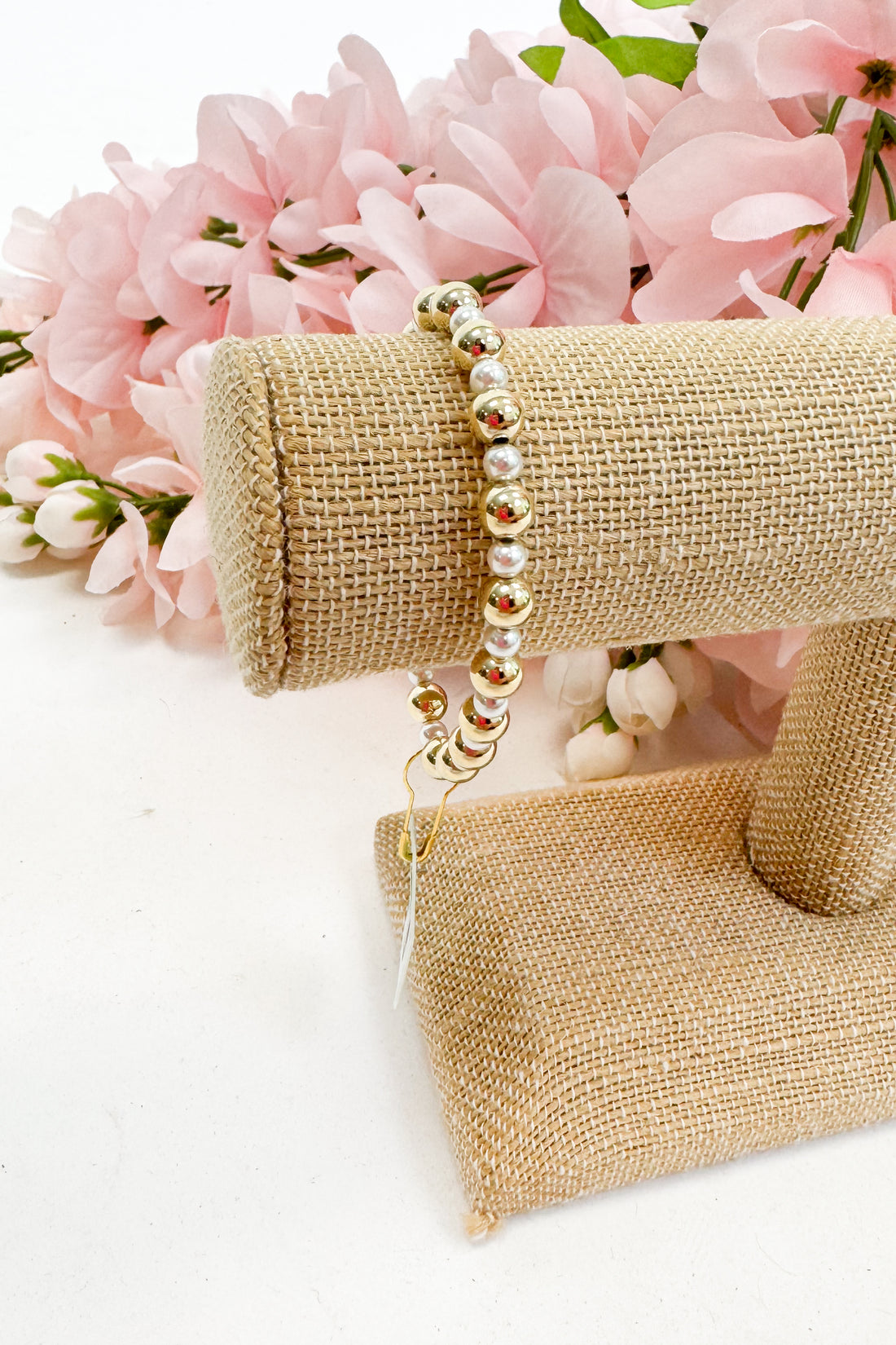 Pearl bracelet on a gold bracelet display with pink flowers in the background