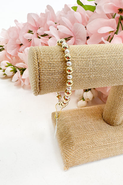 Pearl bracelet on a gold bracelet display with pink flowers in the background