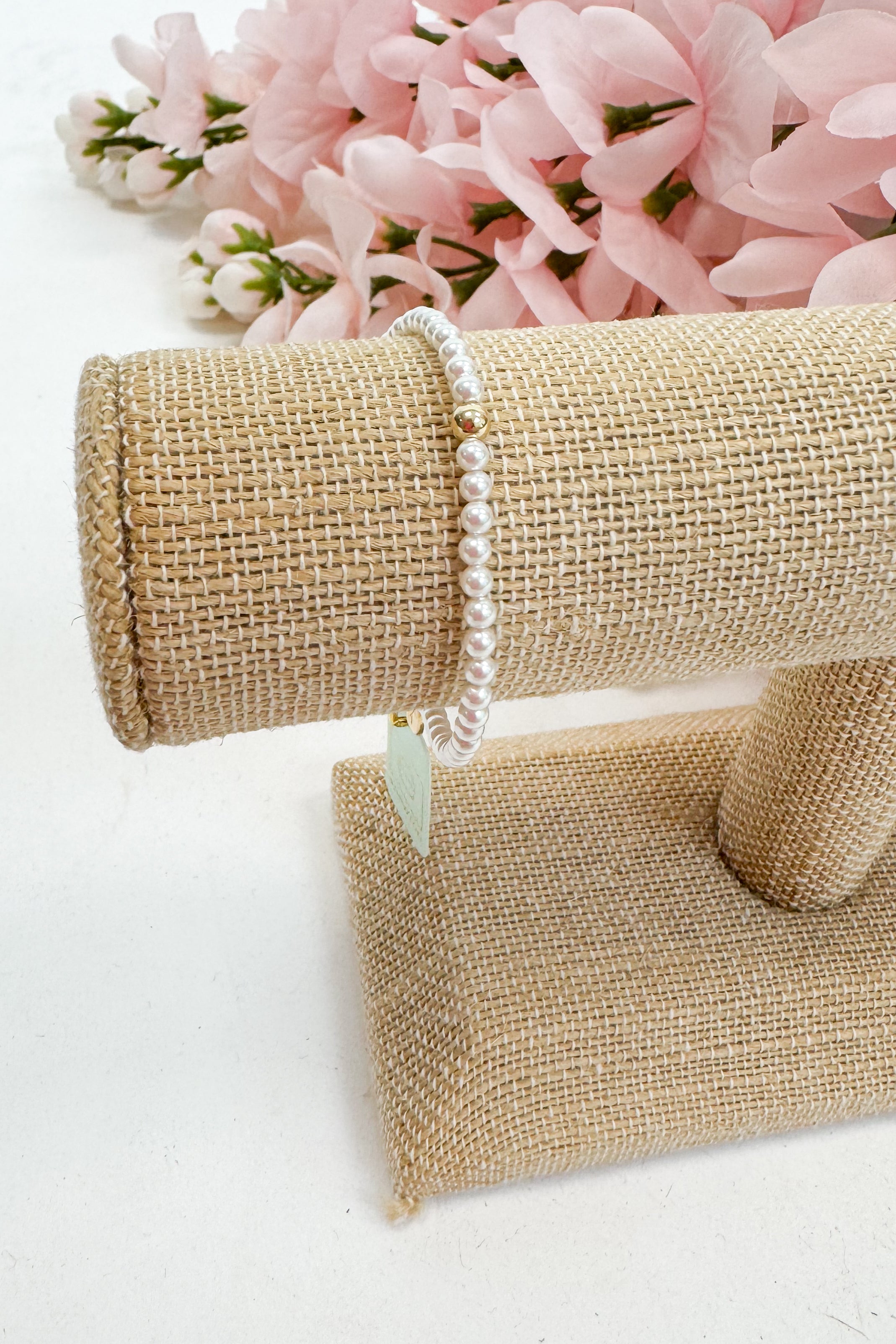 Pearl bracelet on a burlap stand with pink flowers in the background
