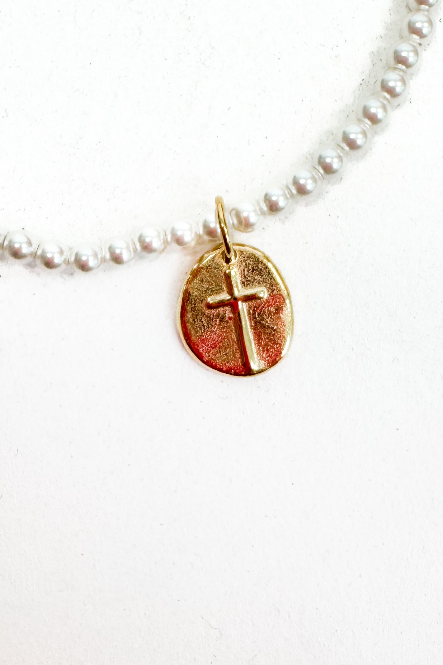 Gold cross pendant on a pearl bracelet against a white background
