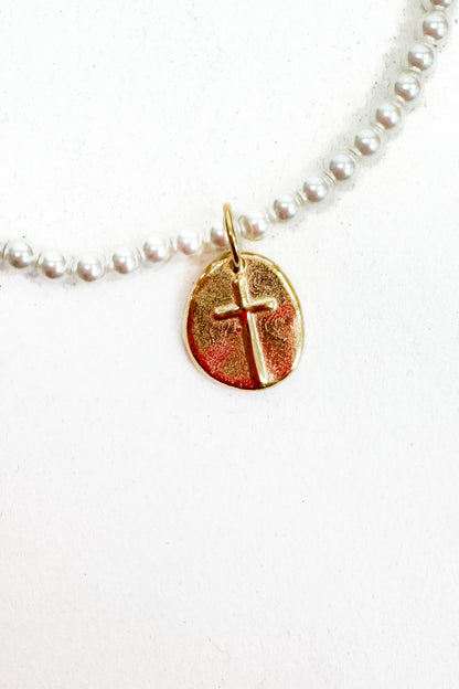 Gold cross pendant on a pearl bracelet against a white background