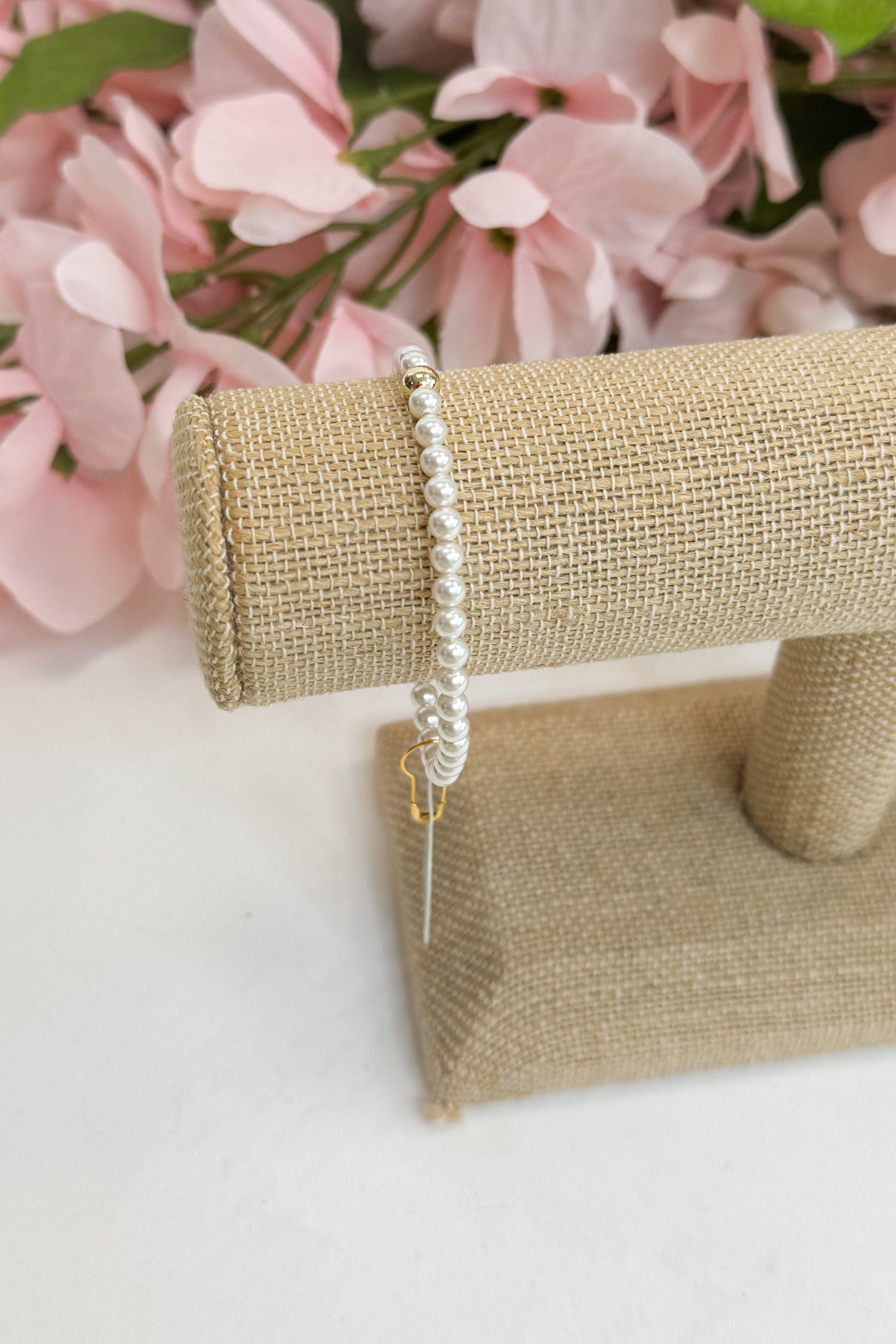 Pearl bracelet on a burlap stand with pink flowers in the background