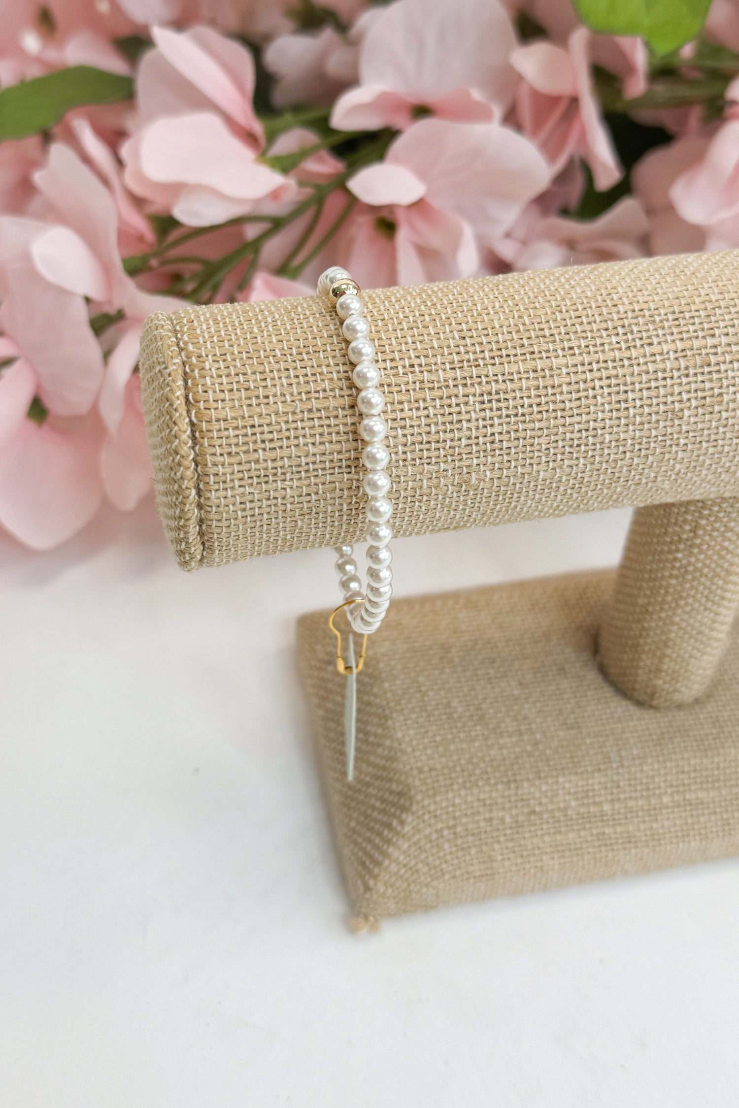 Pearl bracelet on a jewelry stand with pink flowers in the background