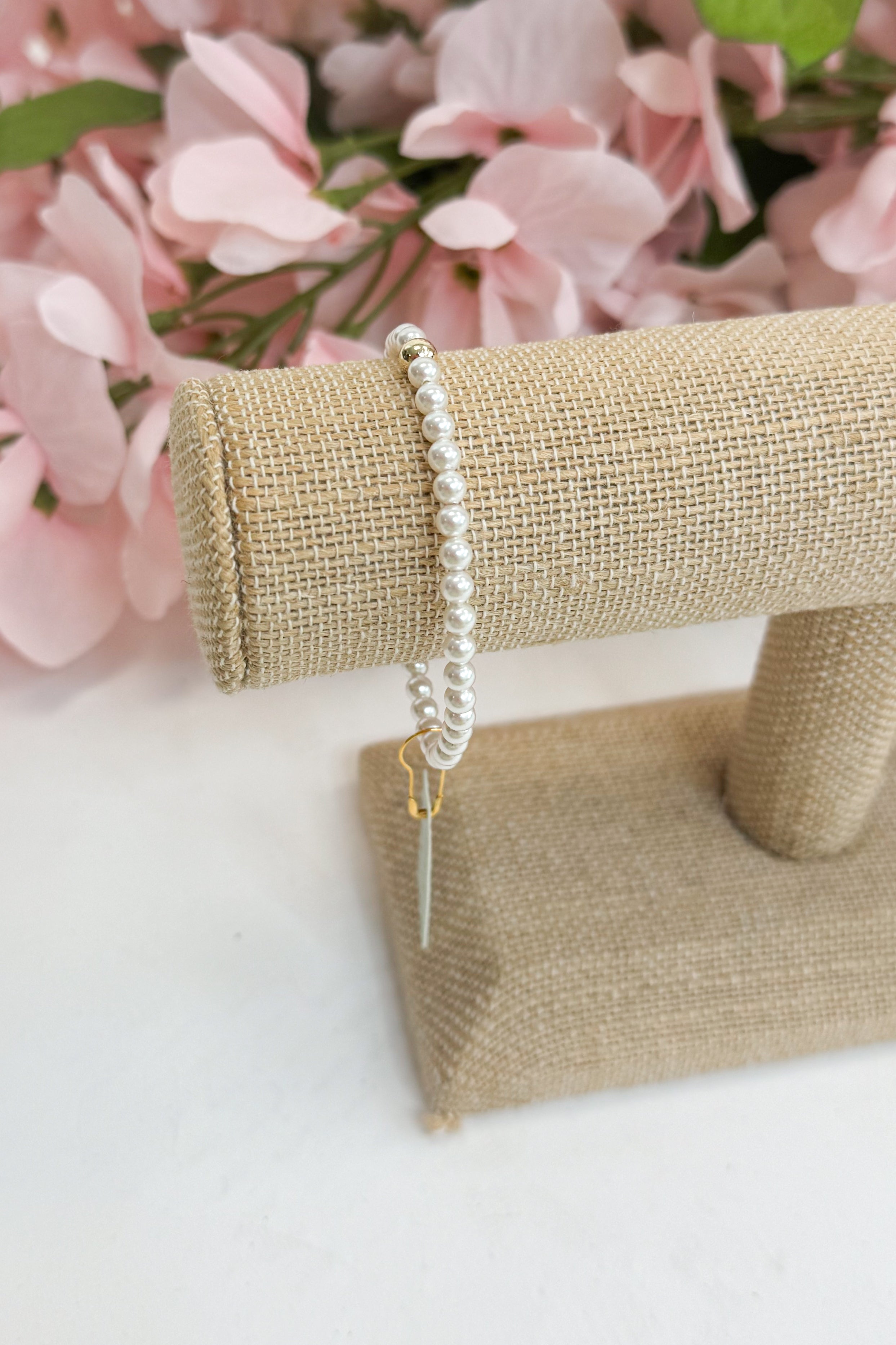 Pearl bracelet on a jewelry stand with pink flowers in the background