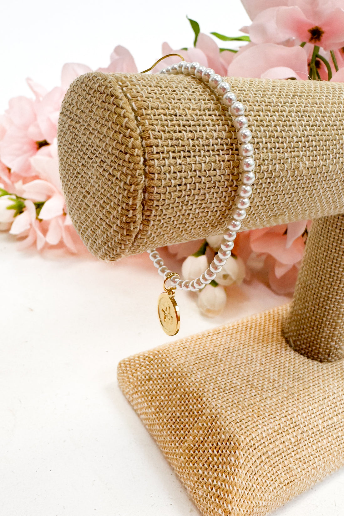 Pearl bracelet on a gold jewelry stand with pink flowers in the background