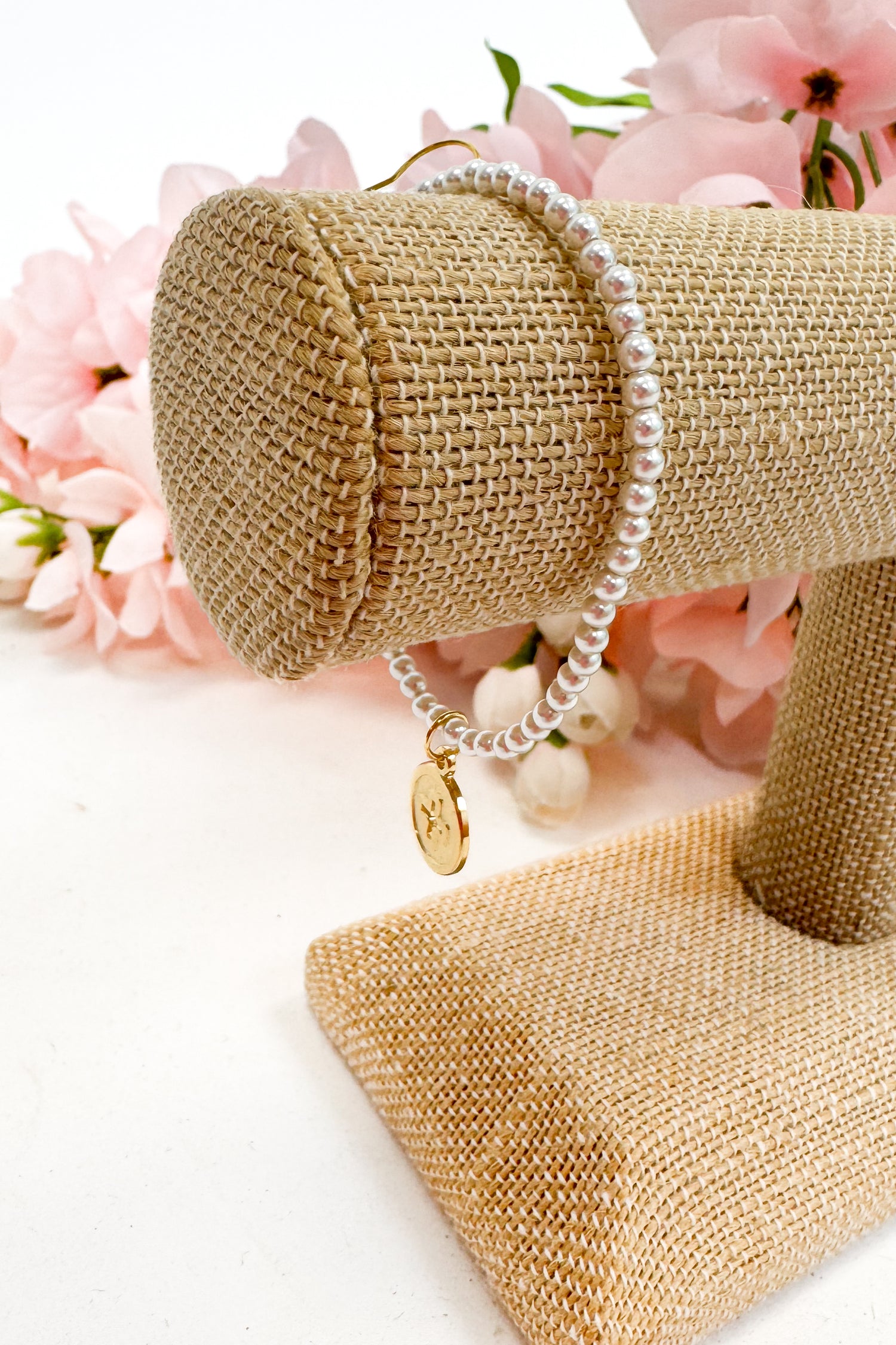 Pearl bracelet on a gold jewelry stand with pink flowers in the background