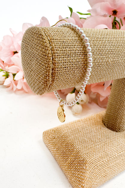 Pearl bracelet on a gold jewelry stand with pink flowers in the background