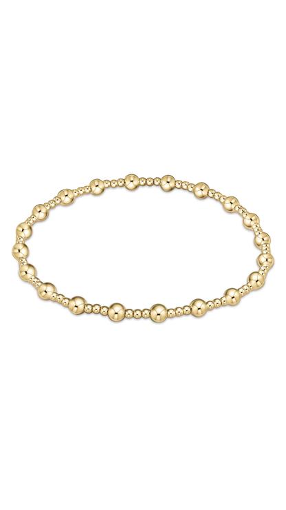 A gold beaded stretch bracelet featuring alternating polished round beads and smaller textured barrel beads, displayed in a horizontal oval shape on a clean white background.