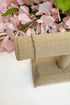 Gold bracelet on a burlap roll with pink flowers in the background