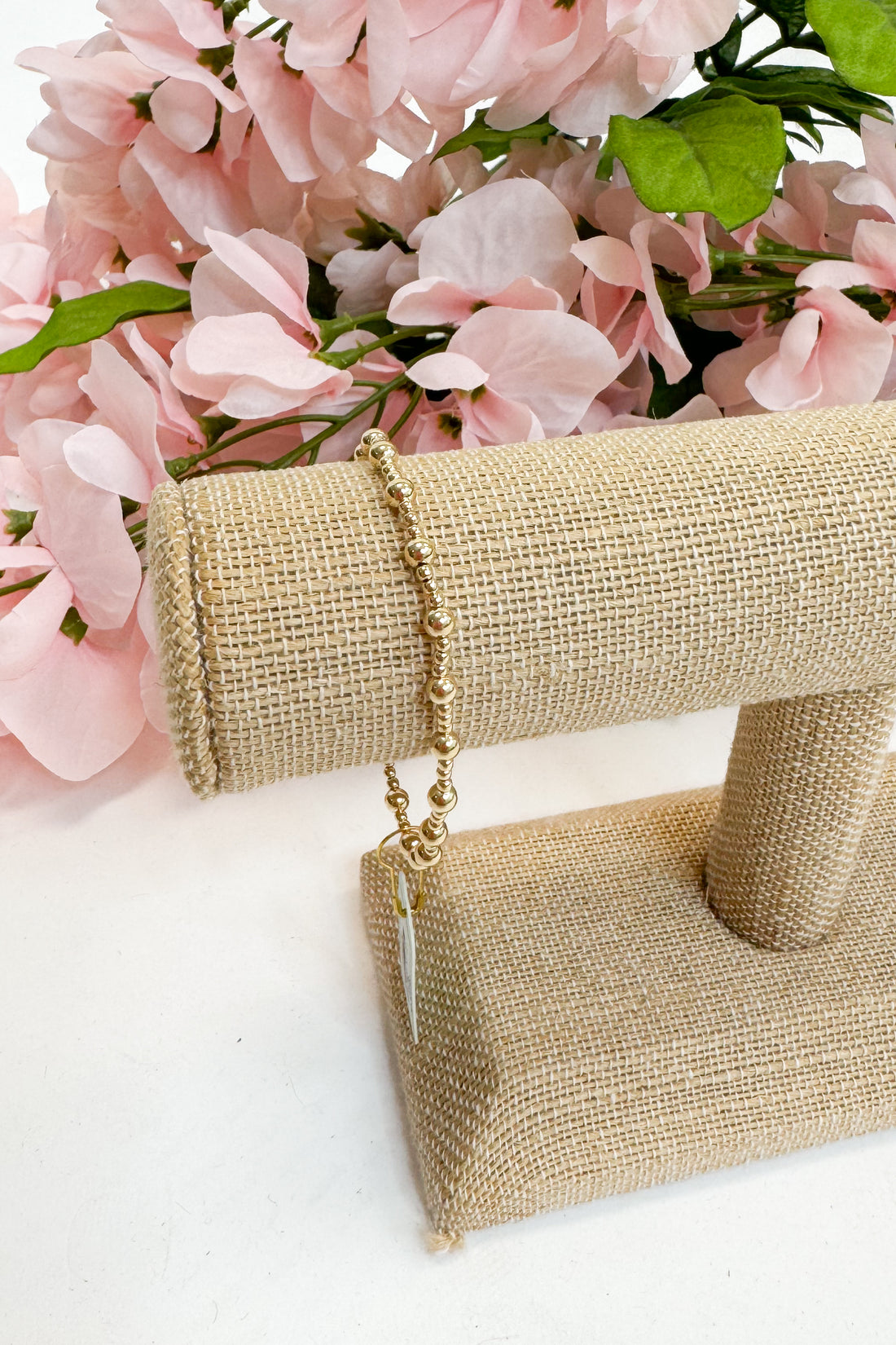 Gold bracelet on a beige stand with pink flowers in the background