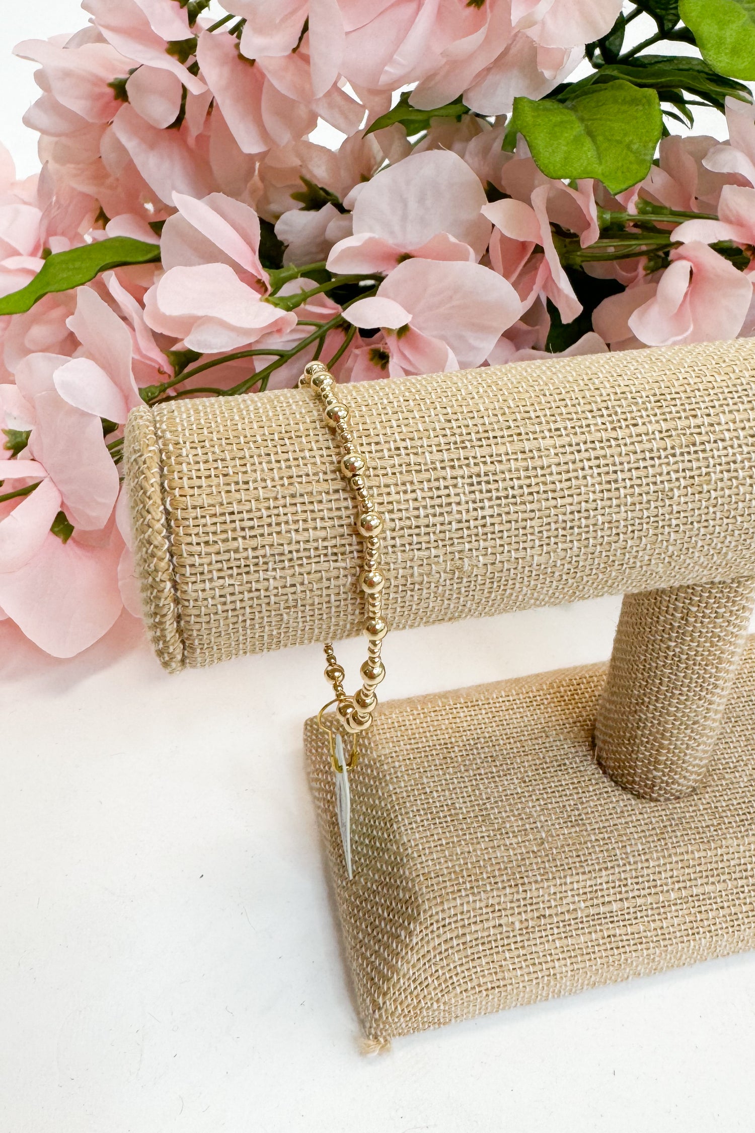 Gold bracelet on a beige stand with pink flowers in the background