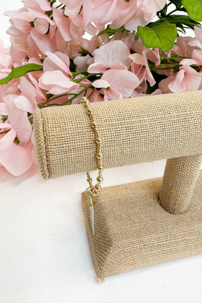 Gold bracelet on a beige stand with pink flowers in the background