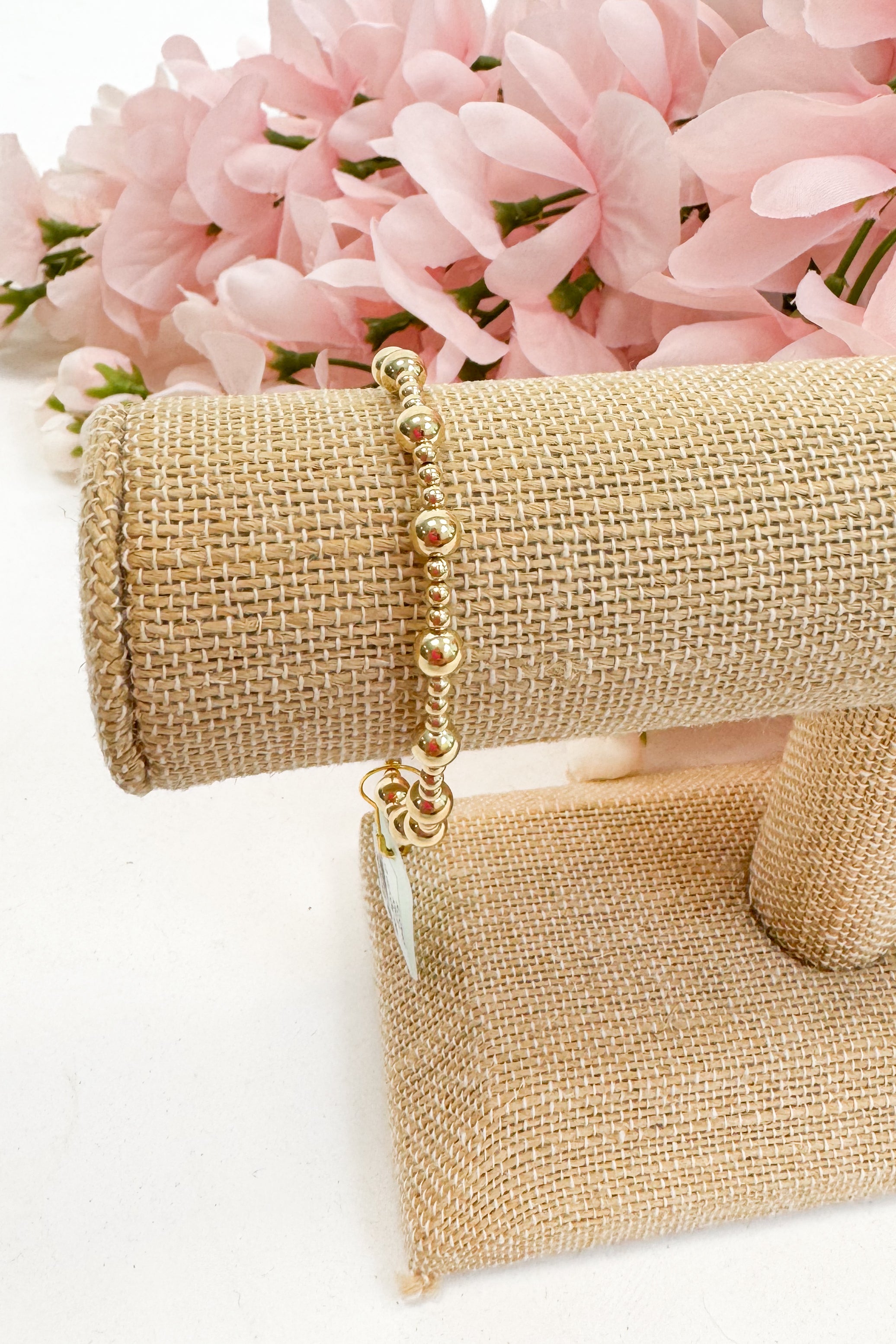 Gold bracelet on a beige jewelry display with pink flowers in the background