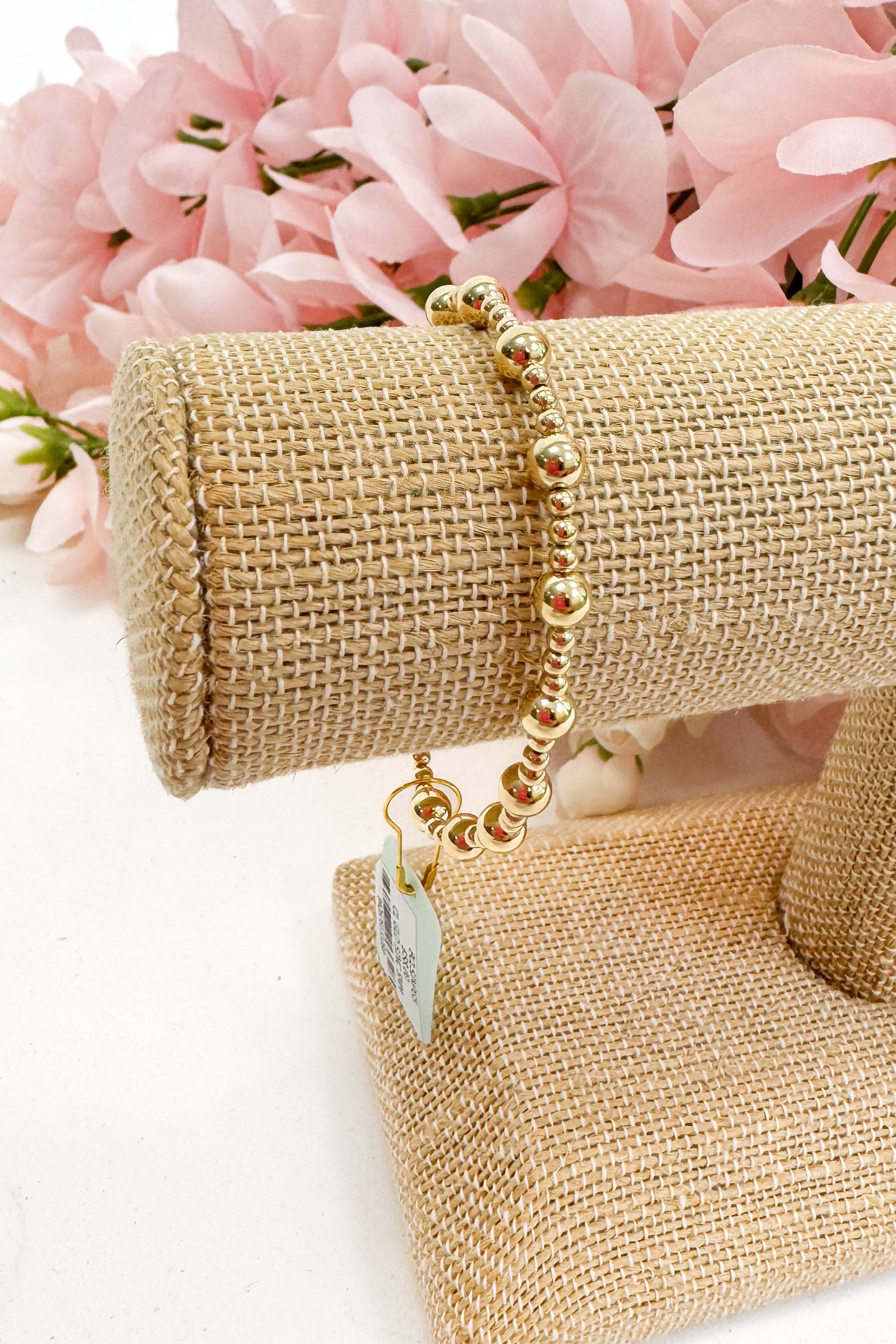 Gold bracelet on a beige jewelry display with pink flowers in the background