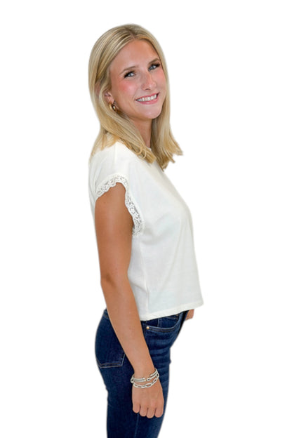 Side view of woman wearing Swagger Boutique’s Cloud Marika Lace Trim Muscle Tee by Z Supply with jeans against white studio background.