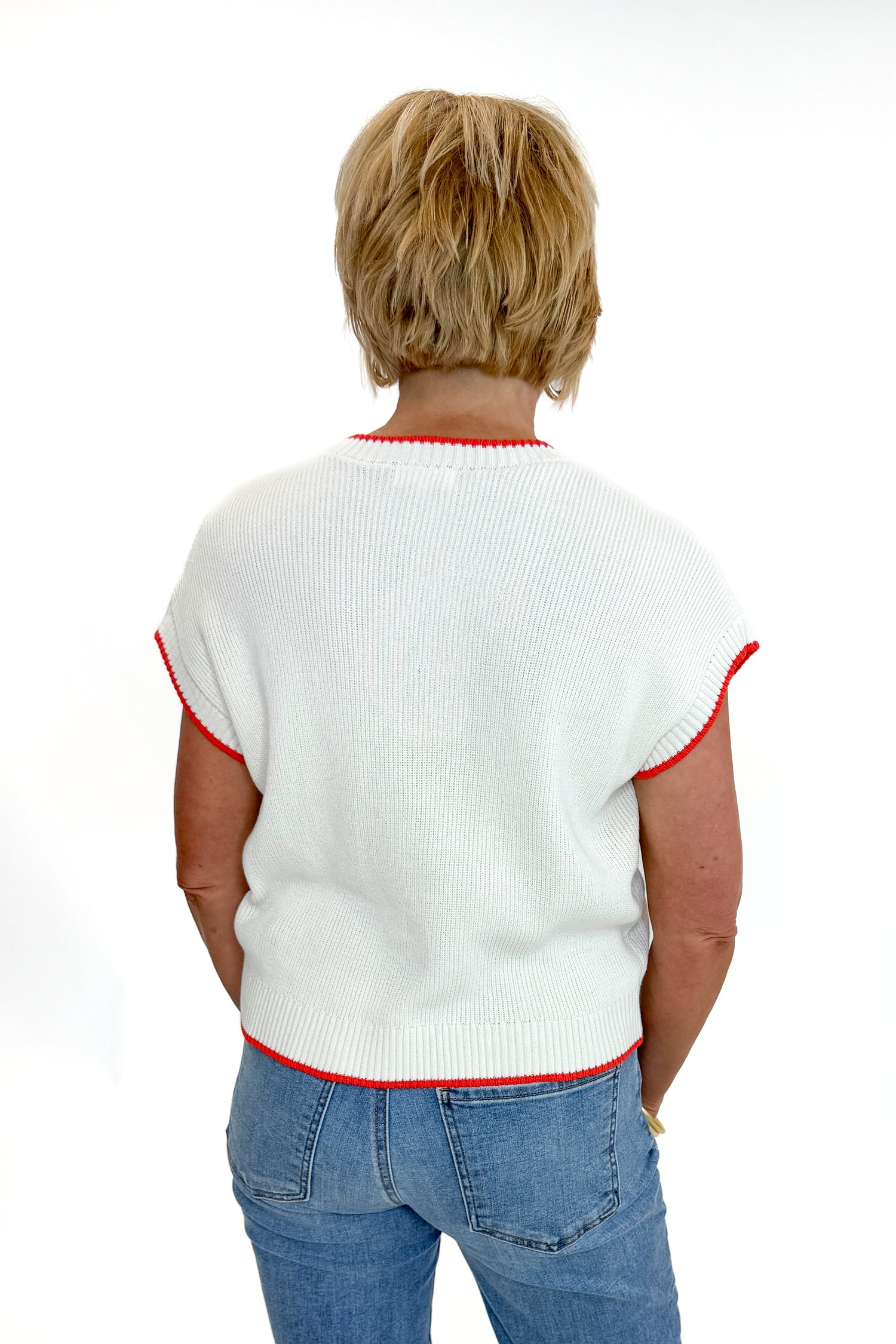 Back view of woman wearing Swagger Boutique’s  Sleeveless Patriot Sweater In Cloud by Z Supply with jeans and sandals against white studio background.