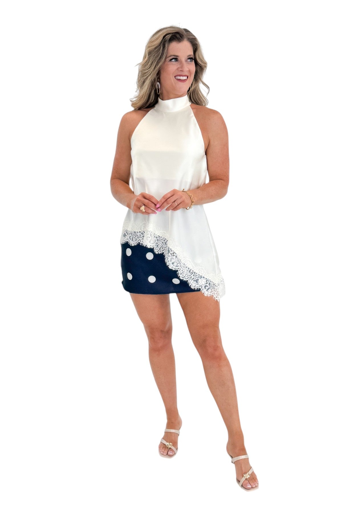 Front view of woman wearing Swagger Boutique’s Cream Asymmetrical Halter Neck Satin Lace Top with polka dot skirt against white studio background.