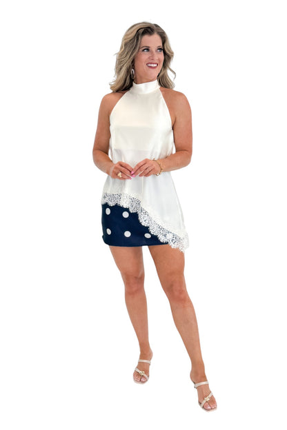Front view of woman wearing Swagger Boutique’s Cream Asymmetrical Halter Neck Satin Lace Top with polka dot skirt against white studio background.