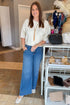 Front view of woman wearing Swagger Boutique’s Cream Button Down Short Sleeve Sweater by PINCH with jeans standing at the store.