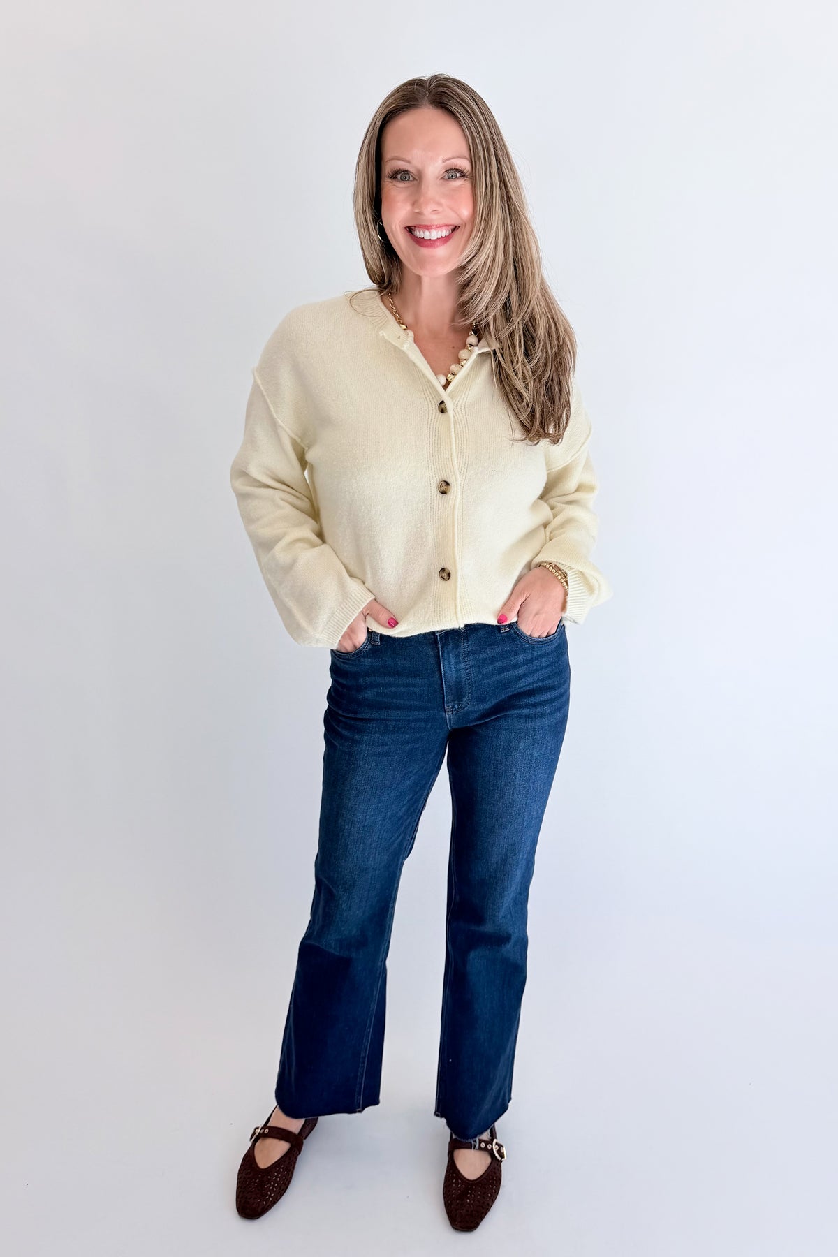 Front view of woman wearing Swagger Boutique’s Cream Button Up Cardigan with jeans against white studio background.