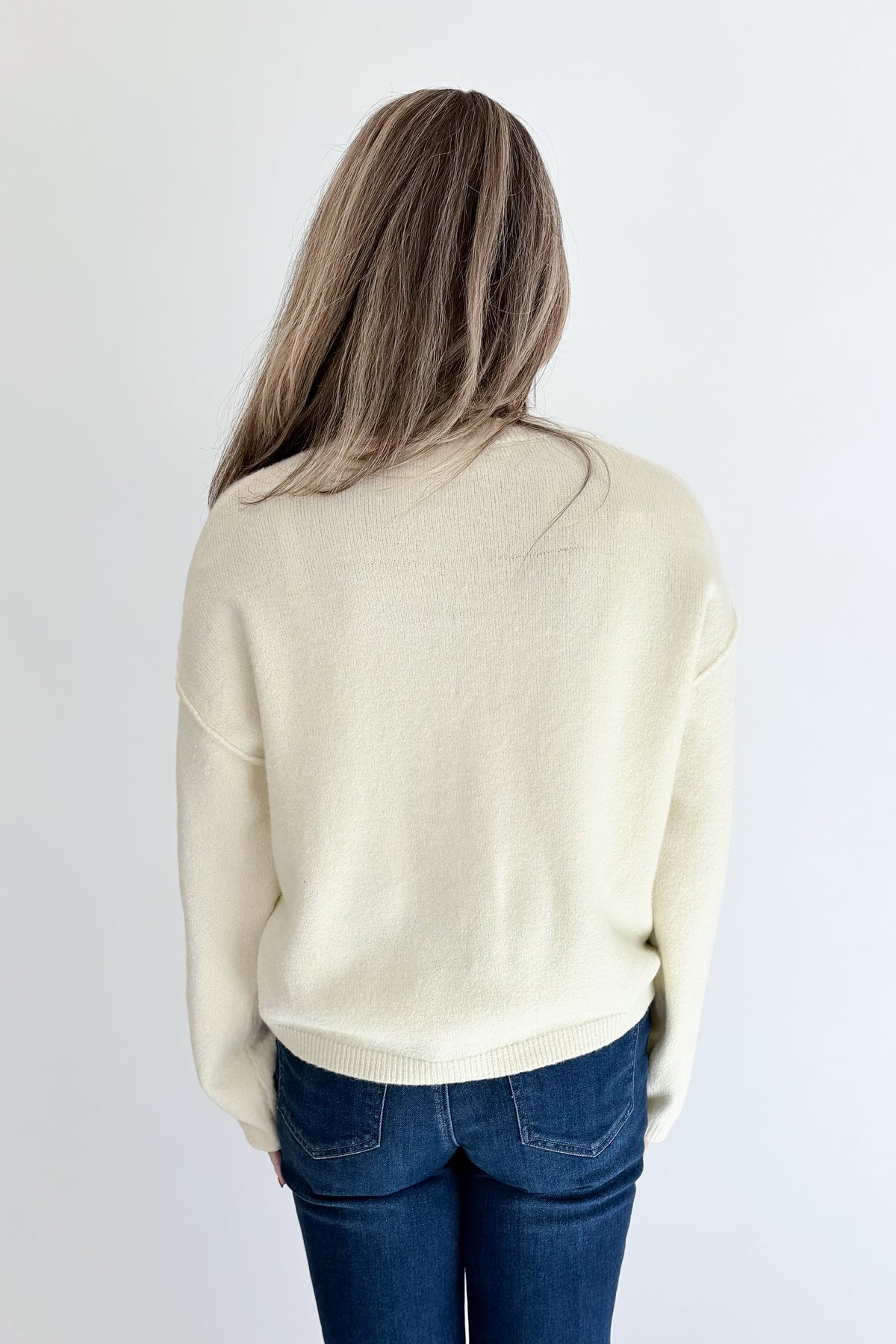 Back view of woman wearing Swagger Boutique’s Cream Button Up Cardigan with jeans against white studio background.