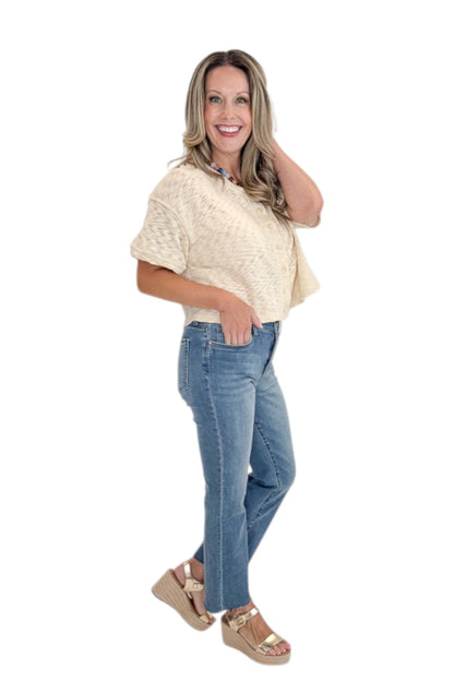 Side view of woman wearing Swagger Boutique’s Cream Button Up Short Sleeve Sweater with jeans against white studio background.