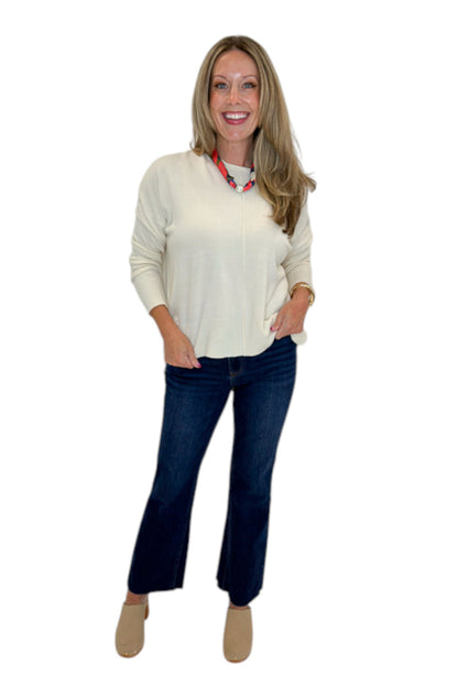 Front view of woman wearing Swagger Boutique’s Cream Center Seam Round Neck Sweater with jeans against white studio background.