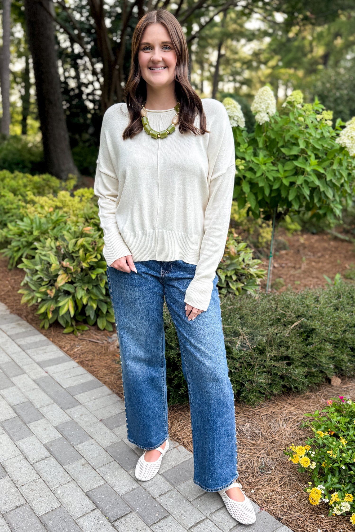 Front view of woman wearing Swagger Boutique’s Cream Center Seam Round Neck Sweater  standing outside on a pathway.