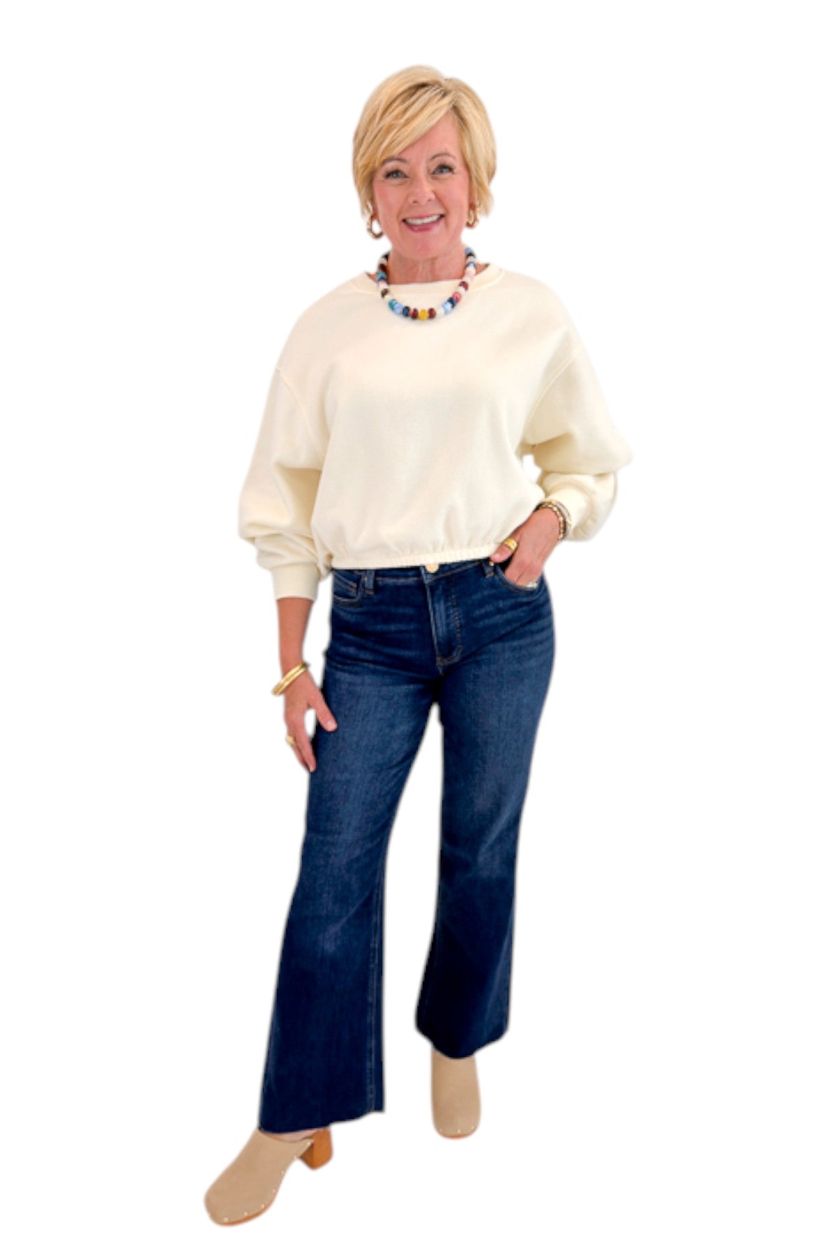 Front view of woman wearing Swagger Boutique’s Cream Elastic Hem Sweatshirt with jeans against white studio background.