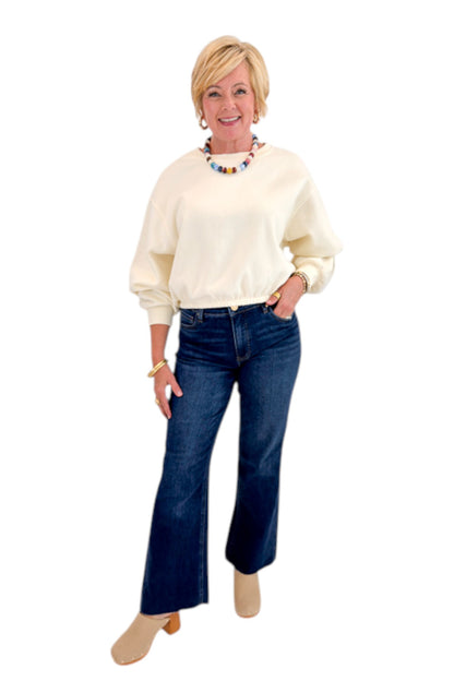 Front view of woman wearing Swagger Boutique’s Cream Elastic Hem Sweatshirt with jeans against white studio background.