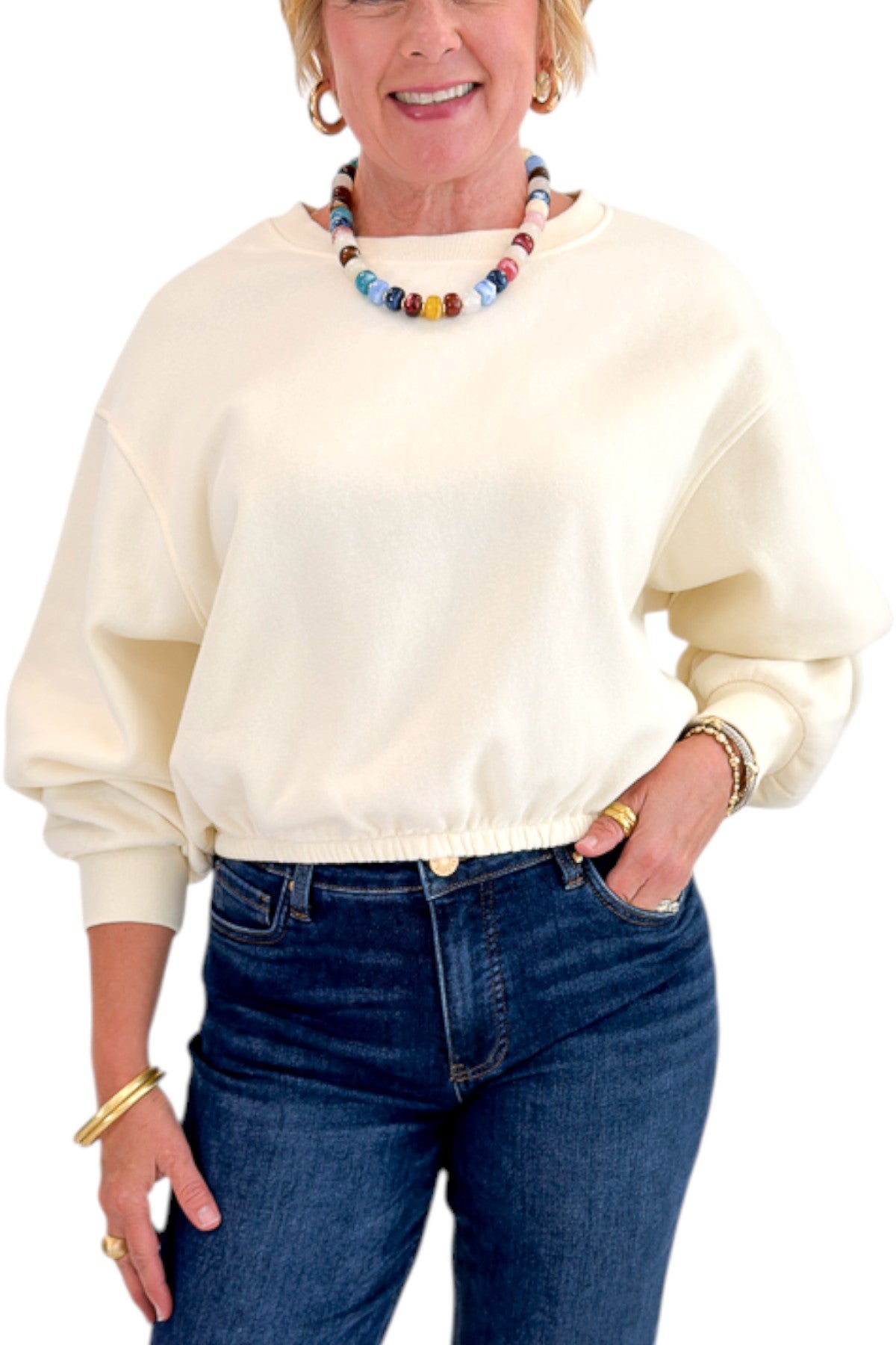Front detail view of woman wearing Swagger Boutique’s Cream Elastic Hem Sweatshirt with jeans against white studio background.