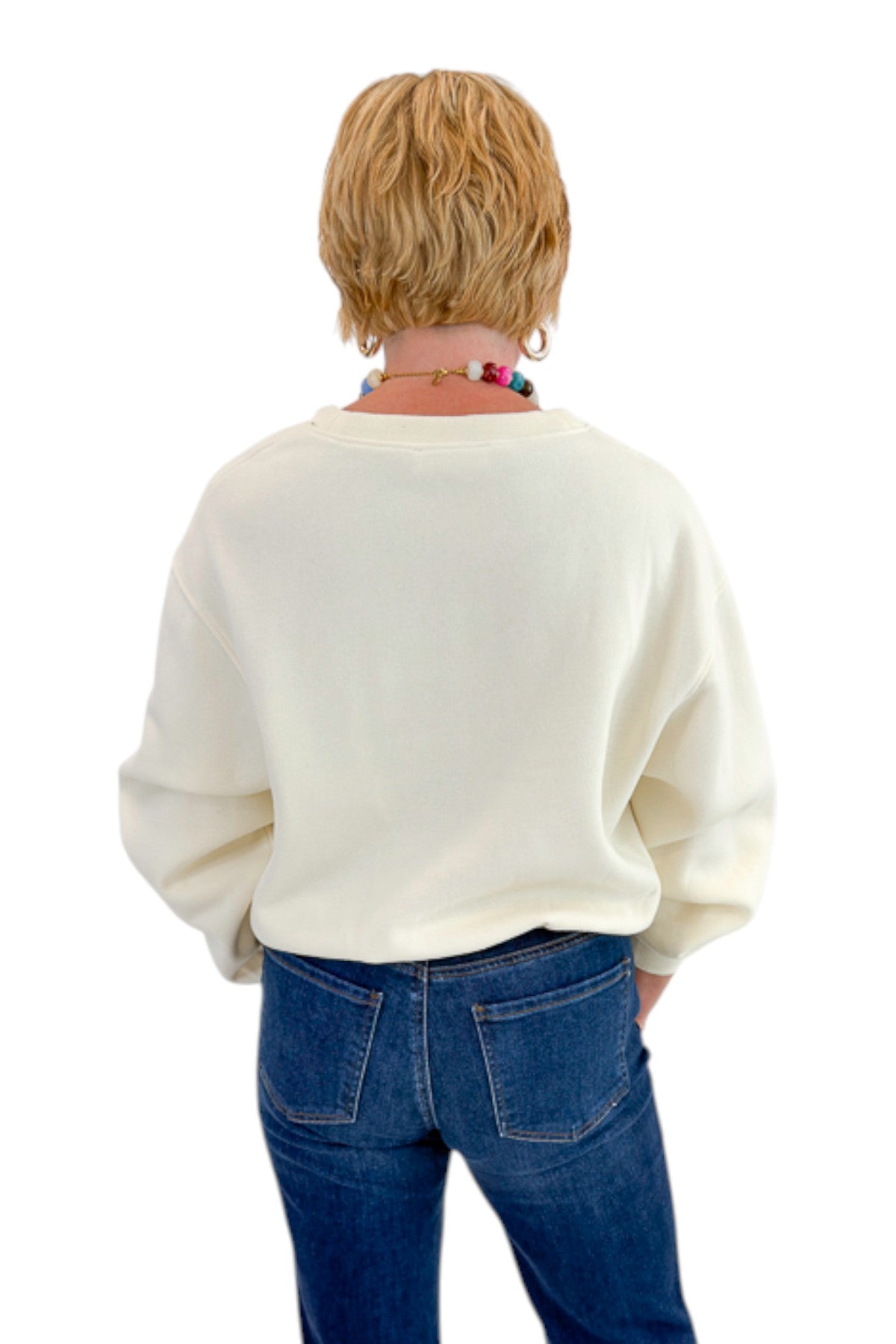 Back view of woman wearing Swagger Boutique’s Cream Elastic Hem Sweatshirt with jeans against white studio background.