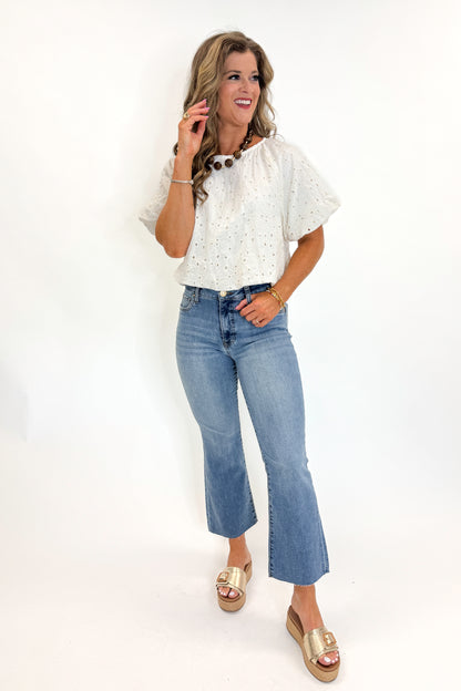 Front view of woman wearing Swagger Boutique’s Cream Eyelet Bubble Hem Top with jeans against white studio background.