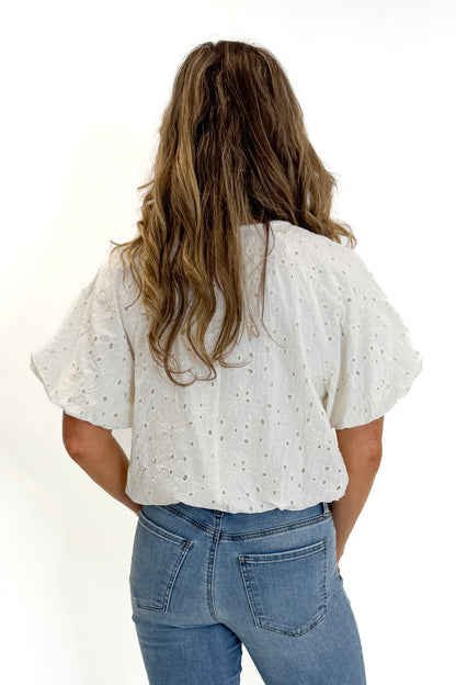 Back view of woman wearing Swagger Boutique’s Cream Eyelet Bubble Hem Top with jeans against white studio background.