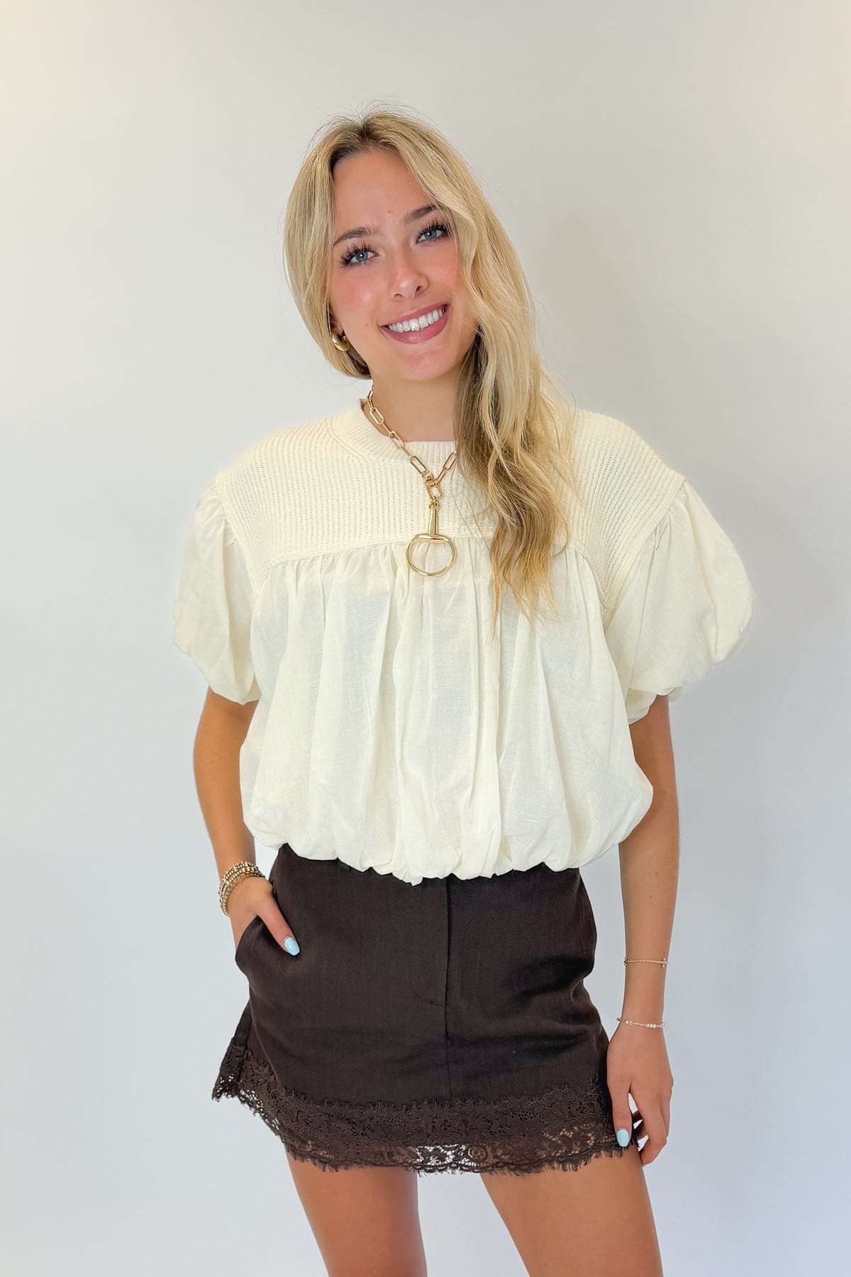 Front view of woman wearing Swagger Boutique’s Brown Lace Lined Denim Skort with Cream Mixed Material Bubble Hem Top against white studio background.