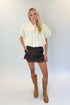 Front view of woman wearing Swagger Boutique’s Brown Lace Lined Denim Skort with Cream Mixed Material Bubble Hem Top against white studio background.